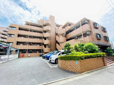 落ち着いた色合いの外観が印象的です。駐車スペースが建物前に確保されています。エントランスまでのアプローチもわかりやすい配置です。緑がほどよく植えられており全体的に明るい雰囲気です。