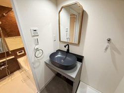 洗面台がアクセントになるデザインで空間に洗練された印象を与えます。シンプルな壁面と調和した鏡が設置されています。蛇口や洗面ボウルの色味が統一され全体としてまとまりがあります。