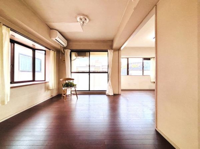 大きな窓があり陽射しがしっかり入るリビングです。エアコン付きで一年中快適に過ごせます。広々とした空間は家具の配置もしやすいです。床の色合いが落ち着いた雰囲気を演出しています。