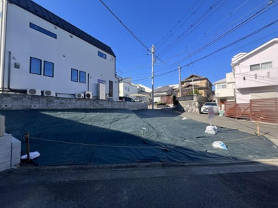 現地土地写真は日当たりのよい開放的な場所で周囲には整った住まいが並んでいます。道路に面しており車の出入りもしやすい環境です。道路との高低差も緩やかで整地された土地が印象的です。