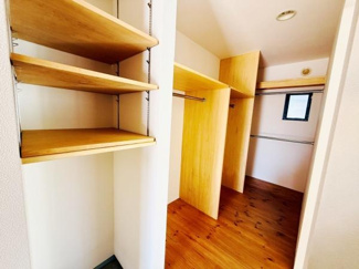 広々としたウォークインクローゼットは収納力が豊富です。棚やハンガーパイプが充実しており整理整頓しやすい設計となっています。奥には窓があり採光にも配慮されています。木目調の床が温かみを感じさせます。