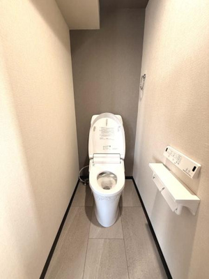 清潔感のあるトイレ空間です。壁紙や床の色調がシンプルで上品な印象を与えます。手元のペーパーホルダーや操作パネルも設置されています。すっきりとしたデザインがポイントです。