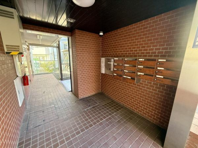 タイル張りのエントランスが落ち着いた雰囲気を演出しています。集合ポストが壁面に設置されており整理された印象です。ガラス扉から自然光が差し込み明るい空間となっています。