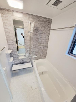 壁面のデザインがアクセントになったバスルームです。大型の鏡が設置されており空間がより広く感じられます。窓があり自然光を取り入れることができます。清潔感のあるシンプルな内装です。