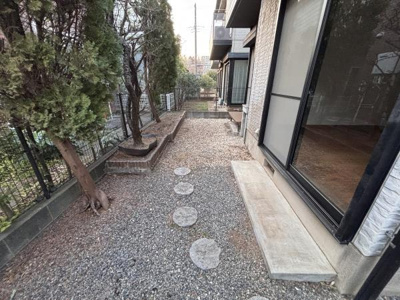 敷地内には玉砂利と飛び石のある庭が広がっています。樹木が植えられた空間でフェンスで囲われた安心感もあります。窓からのアクセスも良好です。石段や花壇スペースも整っています。