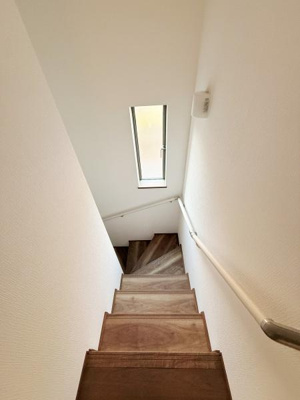 階段エリアにはスリムな縦長の窓があり自然光がしっかりと差し込みます。手すりも設けられているため安心して昇り降りができる仕様です。木目調の階段が落ち着いた印象を与えています。