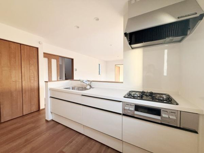 明るく開放感のあるキッチンは白を基調としたデザインで空間がすっきりとしています。シンプルな収納扉が整然と並び作業スペースも広めです。ガスコンロと換気扇が調和し機能性も感じられます。