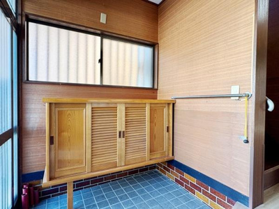 玄関には収納力のある木製シューズボックスが設置されています。窓からの光で玄関内が明るく感じられます。床はタイル仕上げで掃除もしやすく機能的です。壁の木目調が温かい印象を与えます。