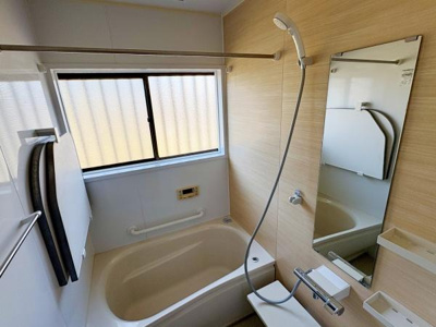 広めの窓が設置されており浴室内に自然光を取り入れることができます。壁面は落ち着いた木目調で清潔感があります。シャワーヘッドやミラー棚などの設備も備えられています。バスタブはゆったりとしたサイズ感です。