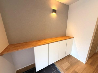 木目調のカウンターと白い扉の組み合わせが印象的な空間です。壁付の照明がアクセントになっています。床の切り替えが空間の印象を引き立てています。収納スペースも充実している点が魅力です。