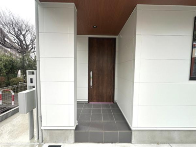 落ち着いた木目調の玄関ドアが住まいに温かみをプラスしています。軒天の木調仕上げが上質な印象を与えます。広めのタイル張りの玄関ポーチが雨の日の出入りも安心です。外壁のホワイトカラーが清潔感を演出します。
