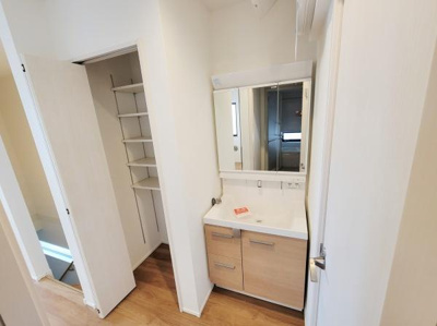 収納棚が備え付けられている洗面台があり使いやすいスペースが確保されています。ナチュラルな色合いの木目調が空間に調和しています。広さもあり日々の身支度が快適に行えそうです。