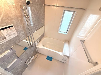 浴室には大きな窓があり明るい空間が広がります。シャワーや手すりも設置され使い勝手に配慮されています。浴槽は広めでゆったりとした印象です。壁面は落ち着いた色合いでまとまっています。