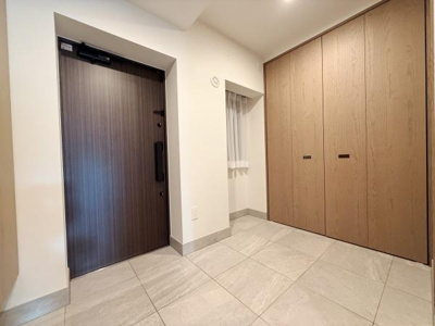 玄関は明るく開放的な空間です。大きめの収納スペースが備わっており使い勝手が良いです。床はお手入れがしやすい素材で清潔感のある印象です。木目調のドアと収納が調和したデザインです。