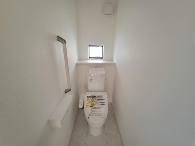 コンパクトで無駄のないトイレ空間です。手すりが設置されており使い勝手も考慮されています。小窓があるため換気もしやすく清潔感があります。明るい内装が印象的です。設備の配置もすっきりとしています。