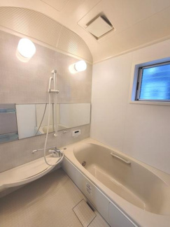 浴室には大きな窓があり自然光を取り入れやすい設計です。シャワーとバスタブが独立して配置されています。壁面のミラーも広く明るい照明が印象的です。空間がすっきりまとまっています。