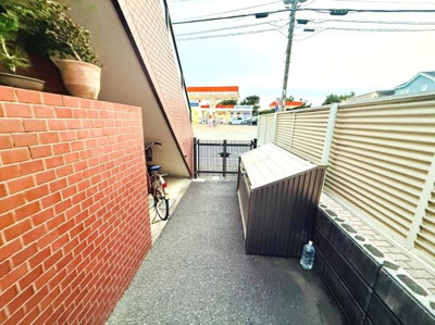 建物横のスペースには自転車や備品の収納に便利な物置が設置されています。前方には門扉があり出入りもスムーズです。周囲のフェンスや塀で外部からの視線にも配慮されています。