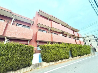 赤レンガ調の外観が印象的な建物です。道路沿いには植栽が整えられています。通りからの視線を遮る工夫が見られます。バルコニーが各住戸についており開放的な雰囲気です。マンションならではの存在感があります。