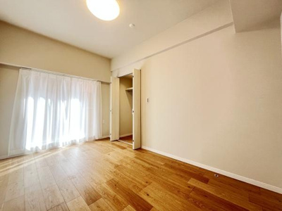 明るい光が差し込む洋室です。ナチュラルな色合いの床とシンプルな内装が特徴です。収納スペースも確保されています。開放感のある空間に仕上がっています。清潔感のある内装が魅力です。