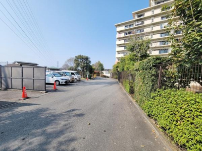 ゆったりとした駐車スペースが確保されており敷地内の緑が周囲に調和しています。道路幅も広く車の出し入れもスムーズに行えます。高層住宅の存在感が印象的な外観です。