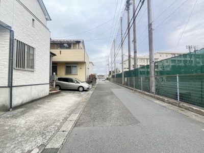 前面道路が広く車の出し入れがしやすい現地写真です。周囲にはフェンスや住居が隣接しすっきりとした街並みが特徴です。道幅も確保されており落ち着いた雰囲気が感じられます。