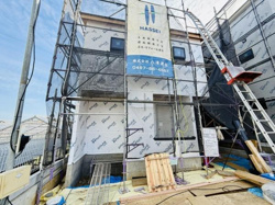 建築途中の建物で足場や建材が並び完成に向けて工事が進行中です。外装下地が丁寧に施工されています。現地の様子が分かりやすく撮影されています。新しい住まいのイメージが膨らみます。