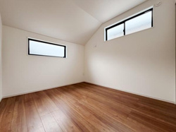 寝室の天井が高く開放感を感じられる空間です。二つの窓から柔らかな光が入ります。木目調の床が落ち着いた雰囲気を演出しています。収納や家具の配置もしやすい間取りです。白を基調とした室内で清潔感があります。