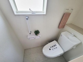 窓からやわらかな光が差し込む明るいトイレです。壁付けの手すりやペーパーホルダーが設置されており使いやすさに配慮されています。タオル掛けもしっかりと設けられていて整頓しやすい空間です。