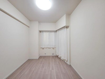 ナチュラルな色合いの洋室です。明るい照明が天井に設置されているため部屋全体がしっかりと照らされています。カーテン付きの窓があり外光も取り入れることができます。床も落ち着いた木目調でまとまっています。