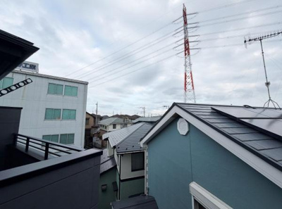 住宅地の屋根や建物が見渡せる眺望です。空が広く感じられ周辺の街並みを確認できます。電線や送電塔も目に入る環境です。周囲の建物との距離も感じられる眺望です。近隣の建物が視界に入り生活の様子が伺えます。