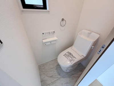 シンプルで清潔感のあるトイレ空間です。窓があり換気しやすい設計となっています。床はお手入れのしやすい素材です。ペーパーホルダーやリモコンも備えられており機能性も備えています。