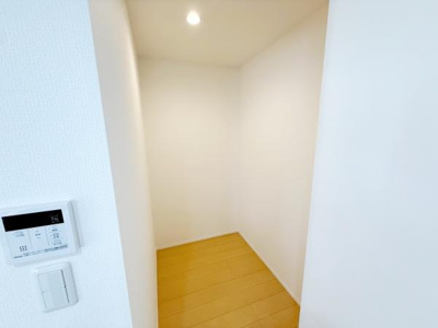 室内にスッキリとした収納スペースがあります。明るい照明が付いていて手元も見やすい仕様です。壁や床はシンプルな色合いで使い勝手に幅が広がります。入口付近にはスイッチ類もまとまっていて便利です。