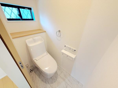 明るい空間に設計され窓から自然光が差し込むトイレです。清潔感のある白を基調としたデザインになっています。収納スペースも確保されており機能的なレイアウトです。壁のリモコン操作で利便性も感じられます。
