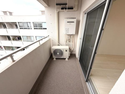 開放感のあるバルコニーです。室外機や給湯器がコンパクトに配置されており空間がしっかり確保されています。隣室との仕切りがシンプルで圧迫感がありません。床面は落ち着いた色合いで整えられています。