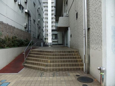 エントランスはゆとりある階段設計でアプローチしやすい点が特徴です。手すりも設置されており安心感があります。タイル貼りの外観が整然とした印象を与えます。周囲の植栽が程よいアクセントになっています。