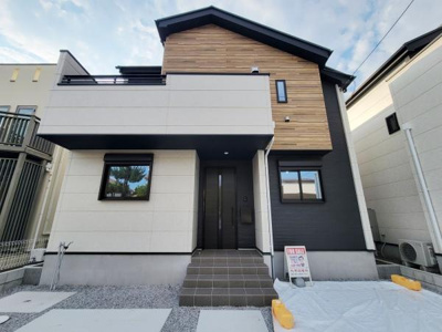 モダンな外観が特徴的な住宅です。シンプルな色使いで洗練された印象を与えます。玄関部分には屋根があり雨の日も安心です。ウッド調のアクセントが温かみをプラスしています。駐車スペースも備わっています。