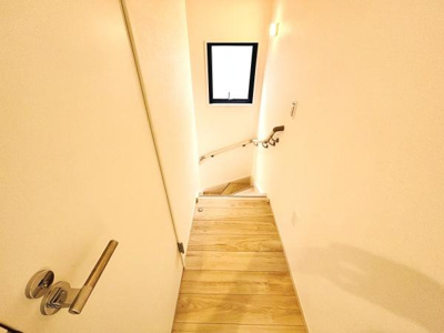 明るい色合いの壁と自然な木目の床が空間をすっきりと見せています。小窓からの採光で階段が明るく保たれています。手すりが設置されているため安心して利用できます。照明がはっきりと照らすため夜間も快適です。