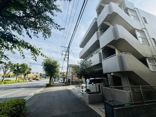 建物の外観が目を引き街路樹が並ぶ前面道路が広がっています。周辺は車通りもありアクセスしやすい環境です。明るい雰囲気の現地写真で建物の佇まいが伝わります。道路幅も十分で通行も快適に行えます。