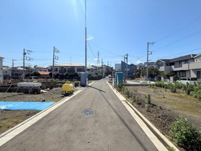 周囲に建物が並ぶ落ち着いた雰囲気の現地写真です。前面道路は広く見通しが良好です。舗装された道路が整備されており車の通行にも安心感があります。建築予定地も隣接している様子が確認できます。