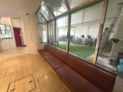 広々としたロビーには長いソファが設置されておりゆったりとした空間が広がっています。大きな窓からは隣接する自転車置き場が見渡せます。エレベーターも近く移動が快適です。明るい雰囲気が特徴的です。