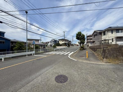 周辺は閑静な住宅街で落ち着いた雰囲気が広がっています。道路幅が広く開放感を感じられます。歩道や横断歩道が整備されており安心して移動できます。坂道の先の景色も印象的です。
