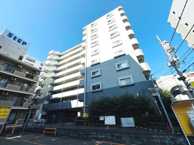 白を基調とした外観が印象的なマンションです。周囲にはビルや施設が立ち並ぶ便利なエリアに立地しています。通りに面した場所に位置しアクセスもしやすいです。建物前には植栽が整えられています。