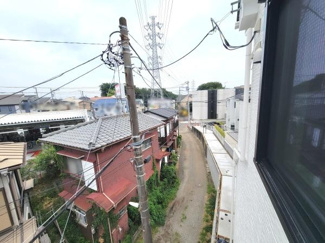 現地からの眺望の写真です。窓から見える周辺の様子を確認できます。近隣の建物や道路の雰囲気を把握しやすい一枚です。電柱や配線も映り現地のリアルな状況が伝わります。ゆったりとした道幅の道路が続いています。