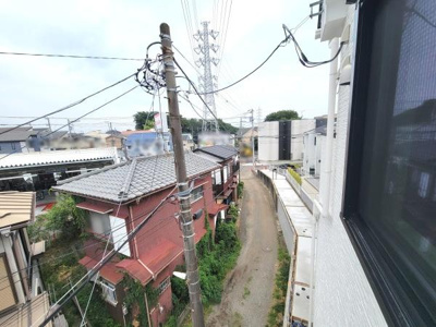 現地からの眺望の写真です。窓から見える周辺の様子を確認できます。近隣の建物や道路の雰囲気を把握しやすい一枚です。電柱や配線も映り現地のリアルな状況が伝わります。ゆったりとした道幅の道路が続いています。