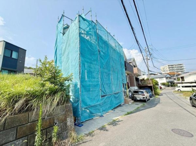 現地の前面道路は広さがあり車の出入りがしやすい環境です。建物は工事中で新築の様子が伺えます。周囲には住宅が立ち並び落ち着いた街並みが印象的です。敷地周辺の植栽も管理されています。