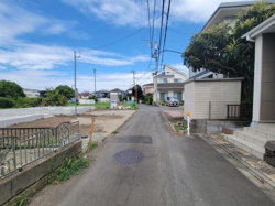 前面道路は見通しが良く交通量も比較的少ないため落ち着いた雰囲気です。周囲には住宅が立ち並び整然とした街並みが感じられます。空も広く開放的な印象の現地写真です。舗装された道路で安心感があります。