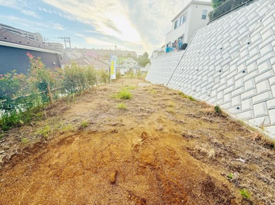 ゆったりとした敷地が広がっており周囲には明るい空間が感じられます。隣接する高い擁壁が特徴的でプライバシーも確保されています。周囲の住宅街の雰囲気も穏やかです。敷地の形状や高低差も個性的なポイントです。