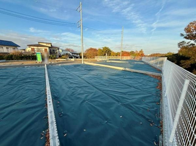 広々とした現地土地写真です。周囲には住宅が立ち並び落ち着いた雰囲気が感じられます。道路やフェンスも整備されており開放感があります。日当たりも良好です。