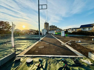 現地から前面道路までのアクセスが分かりやすい写真です。周囲には住宅や高層の建物も見え街並みの様子が伝わります。道幅も確保されており車両の通行も安心感があります。日当たりの状況もしっかり確認できます。