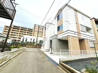 現地の建物はすっきりとした外観が印象的です。前面道路は幅員があり車の出入りがしやすく感じられます。周辺にはマンションなども立ち並び住宅街の落ち着いた雰囲気です。